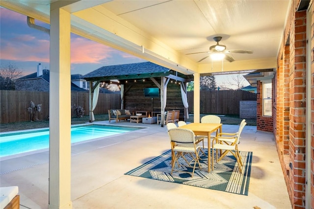 pool at dusk with an outdoor living space, ceiling fan, and a patio