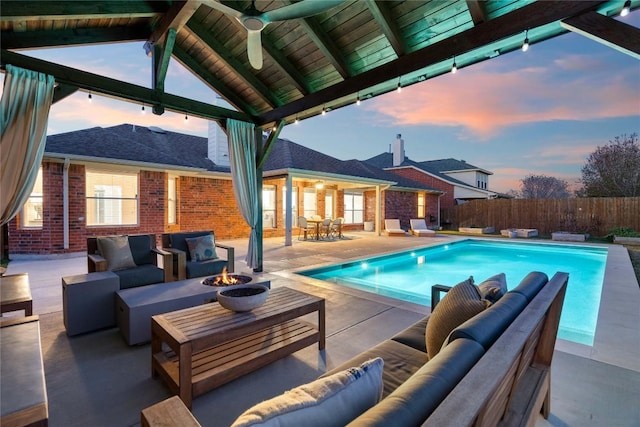 pool at dusk with a gazebo, a patio area, ceiling fan, and an outdoor living space with a fire pit