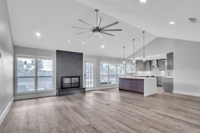 unfurnished living room featuring light wood-type flooring, vaulted ceiling, ceiling fan, sink, and a fireplace