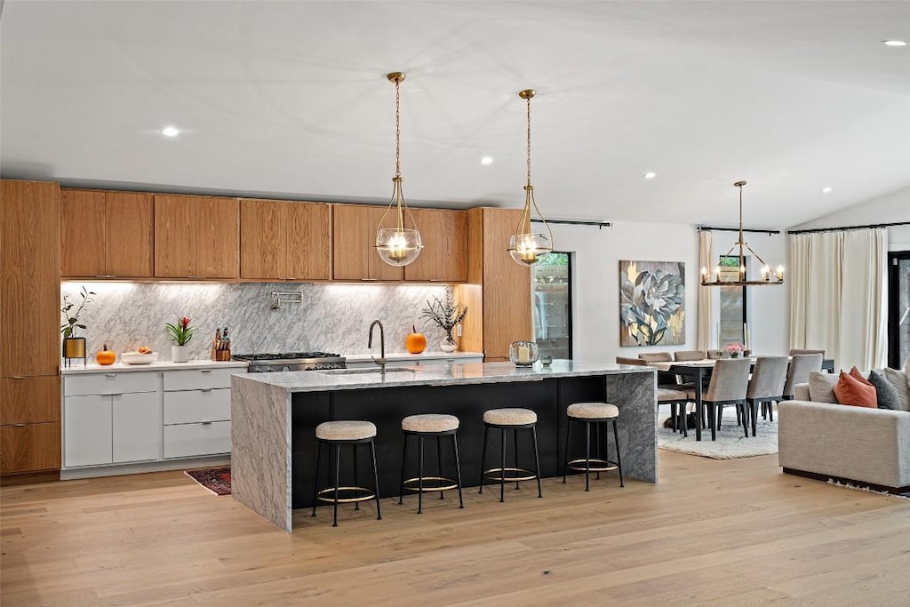 kitchen featuring light stone countertops, sink, decorative light fixtures, white cabinets, and an island with sink