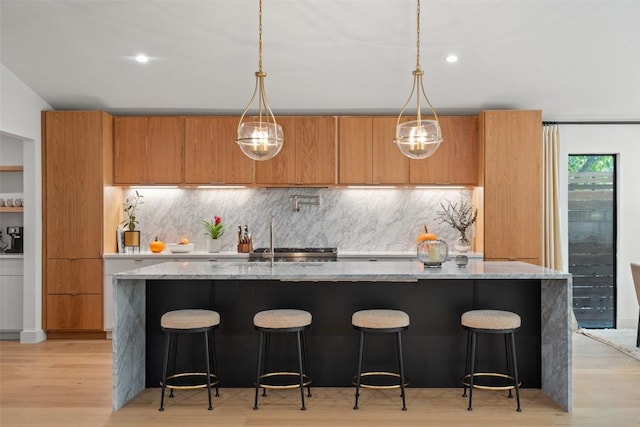 kitchen with sink, light stone counters, an island with sink, decorative backsplash, and light wood-type flooring