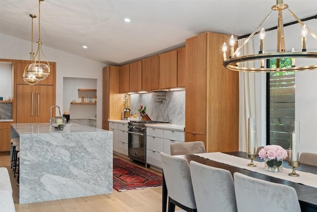 kitchen with backsplash, a center island with sink, vaulted ceiling, stainless steel range, and decorative light fixtures