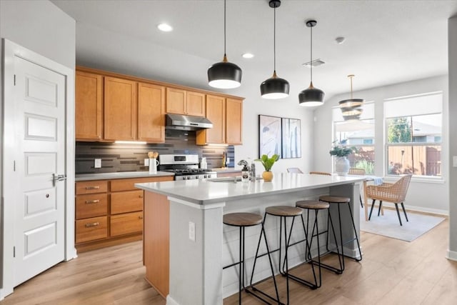 kitchen featuring sink, stainless steel range with gas cooktop, an island with sink, pendant lighting, and decorative backsplash