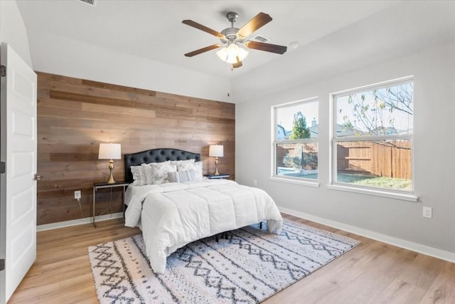 bedroom with ceiling fan, wooden walls, and light hardwood / wood-style flooring