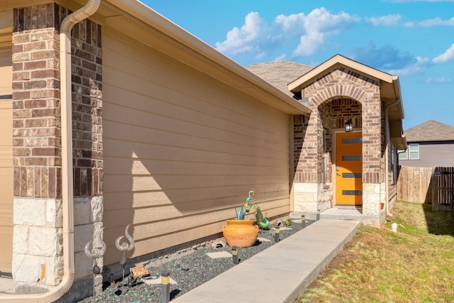 entrance to property featuring a shingled roof, fence, and brick siding