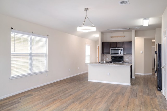 12110 Riprap Dr, Manor, TX 78653 - kitchen with stainless steel microwave, black / electric stove, freestanding refrigerator, tasteful backsplash, and dark brown cabinetry
