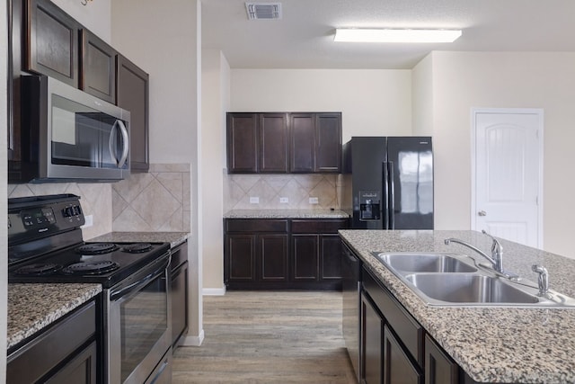 12110 Riprap Dr, Manor, TX 78653 - kitchen featuring stainless steel appliances, a sink, light wood-style floors, dark brown cabinets, and backsplash