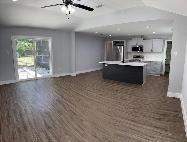 kitchen featuring dark wood-type flooring, a center island with sink, vaulted ceiling, decorative backsplash, and appliances with stainless steel finishes