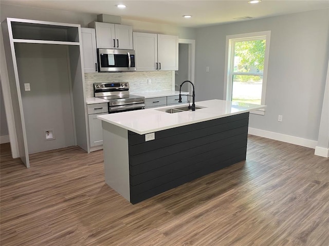 kitchen with a center island with sink, sink, stainless steel appliances, and dark wood-type flooring