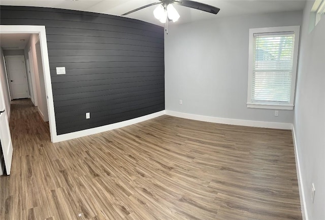 empty room featuring ceiling fan, wooden walls, and wood-type flooring