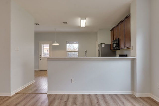 kitchen featuring sink, kitchen peninsula, stainless steel fridge, decorative light fixtures, and light wood-type flooring