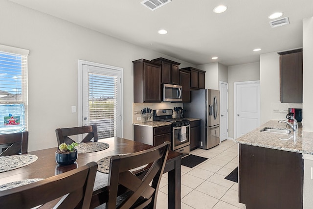 kitchen featuring dark brown cabinetry, sink, light stone counters, light tile patterned floors, and appliances with stainless steel finishes