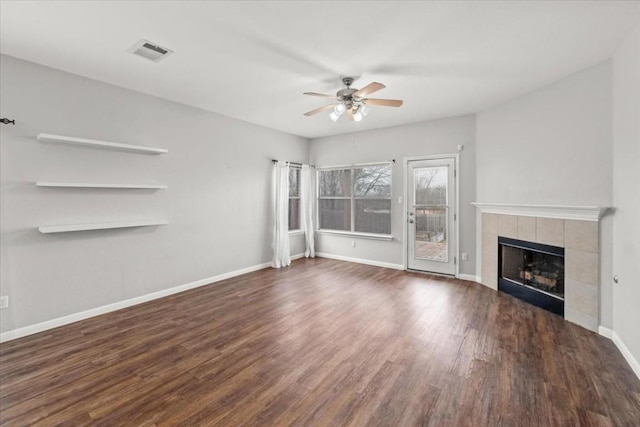 unfurnished living room with a tile fireplace, ceiling fan, and dark wood-type flooring