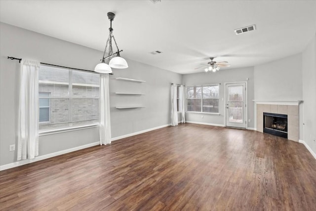 unfurnished living room with a tile fireplace, ceiling fan, plenty of natural light, and dark hardwood / wood-style floors