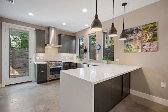 kitchen featuring kitchen peninsula, decorative backsplash, wall chimney exhaust hood, high end stainless steel range oven, and pendant lighting