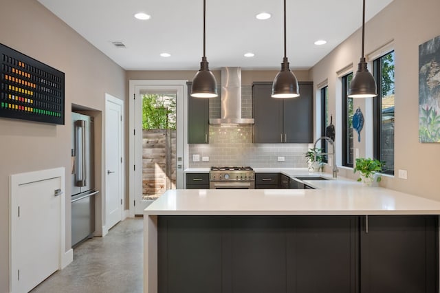 kitchen with sink, hanging light fixtures, high quality appliances, kitchen peninsula, and wall chimney exhaust hood