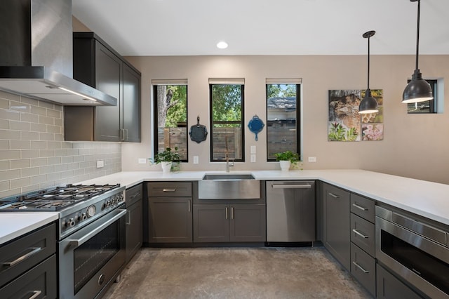 kitchen with tasteful backsplash, stainless steel appliances, sink, wall chimney range hood, and decorative light fixtures