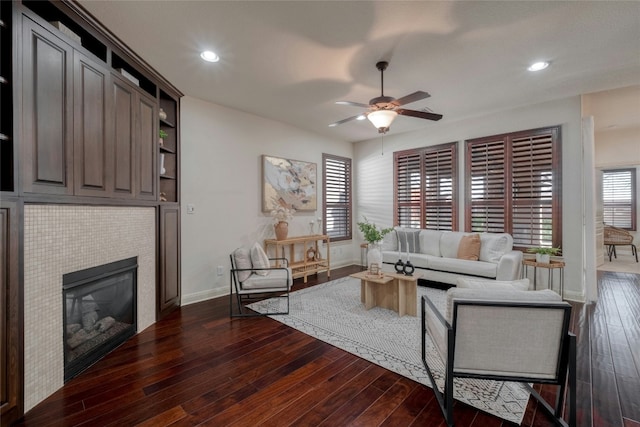 living room featuring a tile fireplace, ceiling fan, and dark wood-type flooring