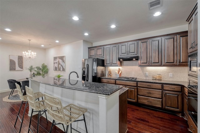 kitchen with a breakfast bar, an inviting chandelier, black appliances, an island with sink, and decorative light fixtures