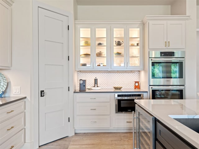 kitchen with stainless steel double oven, beverage cooler, light stone counters, backsplash, and white cabinets