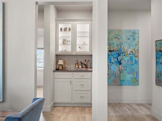 bar featuring decorative backsplash, light wood-type flooring, and white cabinetry