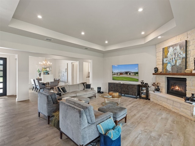 living room with a tray ceiling, a fireplace, an inviting chandelier, and light wood-type flooring