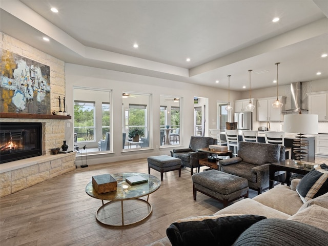 living room featuring a stone fireplace, ceiling fan, and light hardwood / wood-style floors