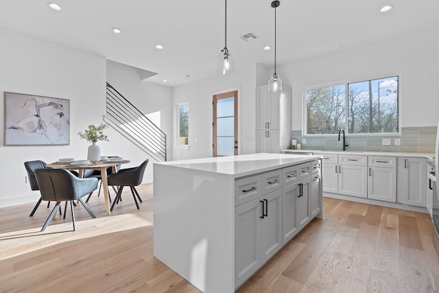 kitchen featuring decorative backsplash, pendant lighting, light hardwood / wood-style flooring, a center island, and white cabinetry