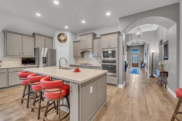 kitchen featuring backsplash, a center island with sink, sink, a kitchen bar, and stainless steel appliances