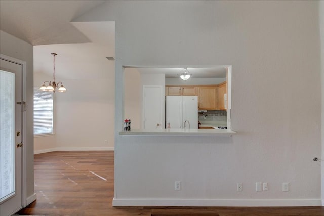 kitchen featuring hardwood / wood-style floors, light brown cabinets, backsplash, an inviting chandelier, and white fridge