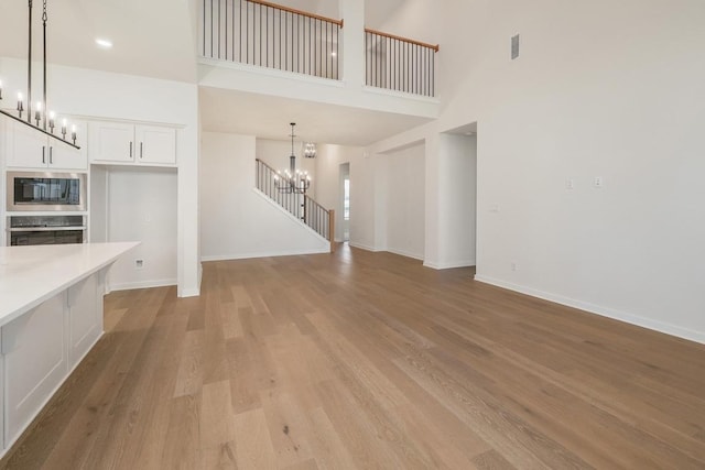 unfurnished living room featuring a notable chandelier, light wood-style floors, baseboards, a towering ceiling, and visible vents