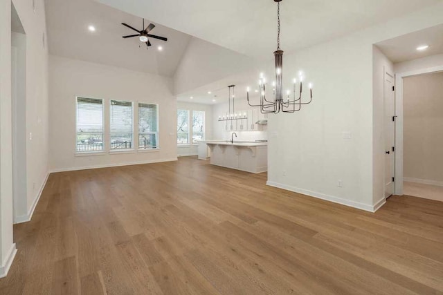 unfurnished dining area with lofted ceiling, baseboards, light wood-style floors, recessed lighting, and ceiling fan with notable chandelier
