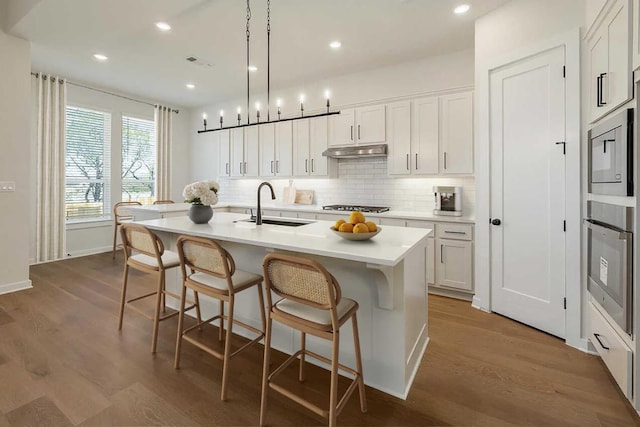 kitchen featuring a breakfast bar area, backsplash, appliances with stainless steel finishes, a sink, and under cabinet range hood
