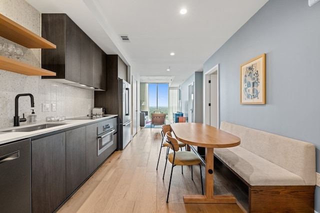 kitchen with sink, light hardwood / wood-style flooring, decorative backsplash, appliances with stainless steel finishes, and dark brown cabinets