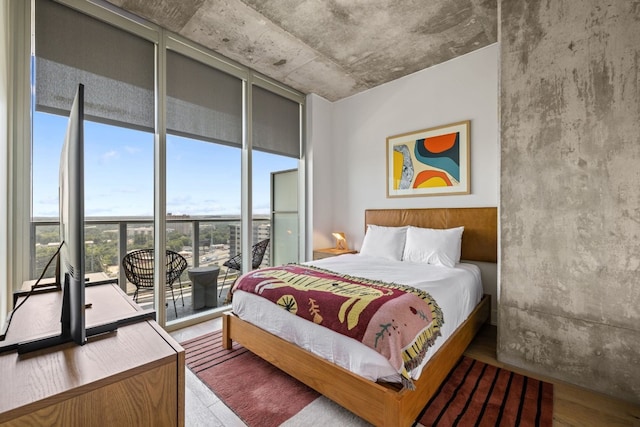 bedroom featuring access to exterior, wood-type flooring, multiple windows, and floor to ceiling windows