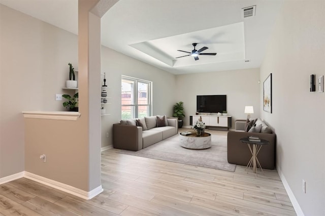 living room with ceiling fan, a raised ceiling, and light wood-type flooring