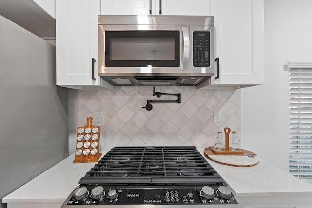 kitchen with tasteful backsplash, white cabinetry, light stone counters, and stove