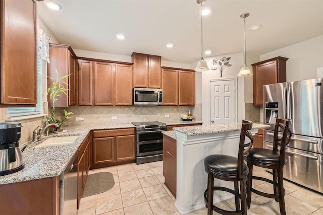 kitchen featuring light stone countertops, sink, hanging light fixtures, a breakfast bar area, and appliances with stainless steel finishes