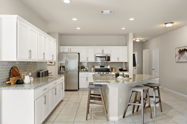 kitchen with light stone counters, stainless steel appliances, light tile patterned floors, white cabinets, and a kitchen island