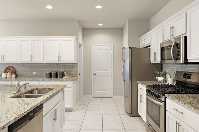 kitchen with light stone counters, stainless steel appliances, sink, white cabinetry, and light tile patterned flooring