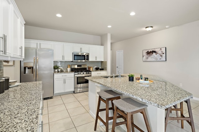 kitchen featuring a kitchen breakfast bar, a kitchen island with sink, white cabinets, and appliances with stainless steel finishes