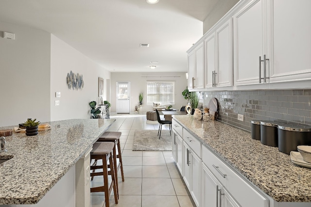 kitchen featuring white cabinets, decorative backsplash, light stone countertops, and light tile patterned flooring