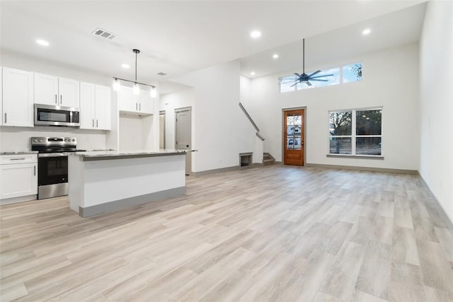 kitchen with a center island, hanging light fixtures, ceiling fan, white cabinetry, and stainless steel appliances