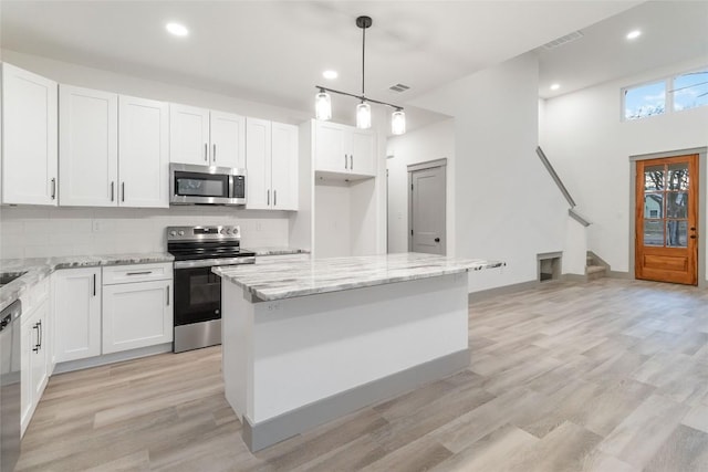 kitchen with white cabinets, appliances with stainless steel finishes, a center island, and decorative light fixtures