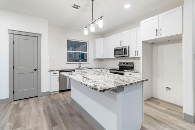 kitchen with appliances with stainless steel finishes, light stone counters, decorative light fixtures, white cabinets, and a kitchen island