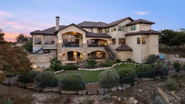 back house at dusk with a patio, a balcony, and a yard