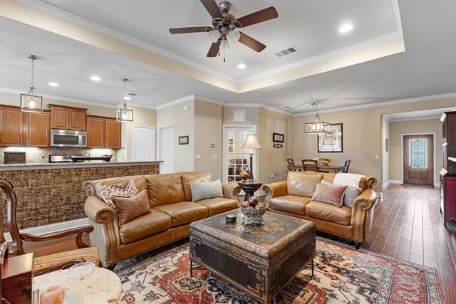 living room with wood-type flooring, ornamental molding, and a tray ceiling