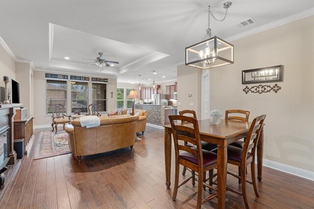 dining area featuring hardwood / wood-style floors, ceiling fan with notable chandelier, a raised ceiling, and crown molding