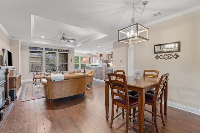 dining space featuring dark wood-type flooring, a tray ceiling, visible vents, and ornamental molding