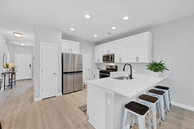 kitchen featuring white cabinetry, sink, kitchen peninsula, a kitchen bar, and appliances with stainless steel finishes